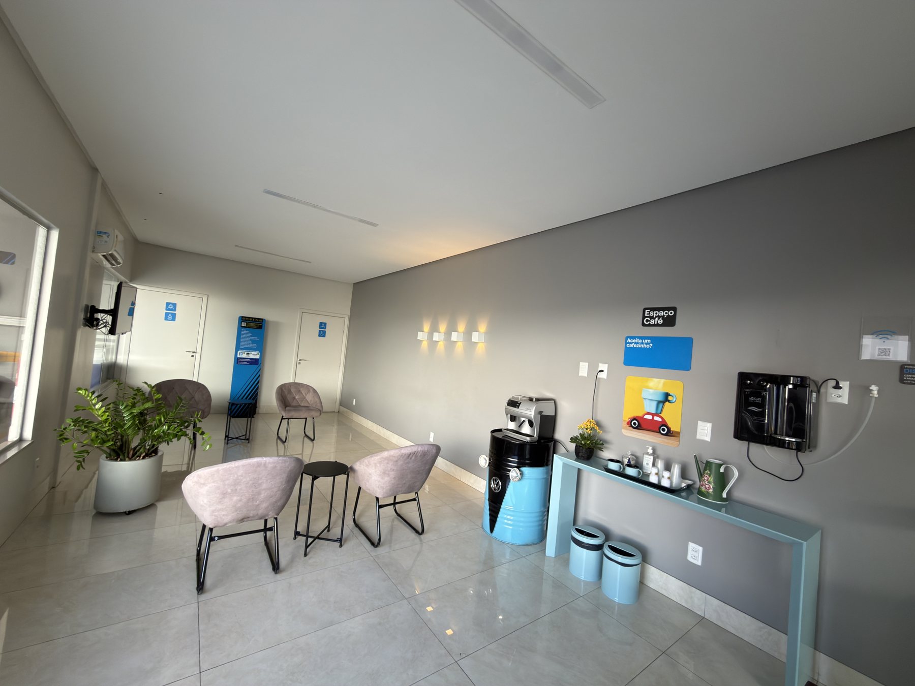 Sala de espera climatizada da oficina, com poltronas, TV, café e água